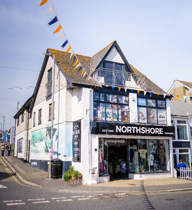 A street view of a white and gray building housing a shop named Northshore, with large display windows, a black sign, and bunting flags hanging above the street under a clear blue sky.